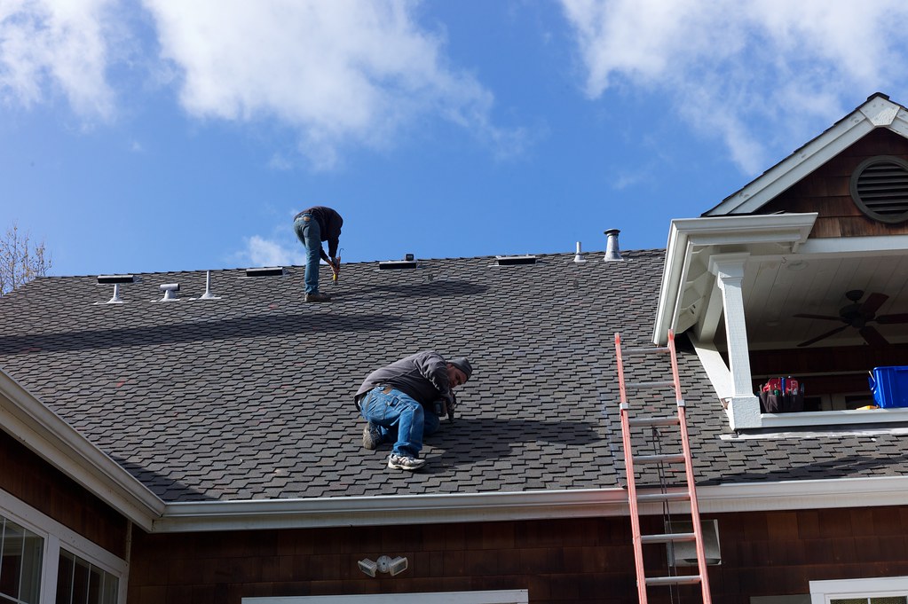 Roofers working on a shingle roof against a clear blue sky